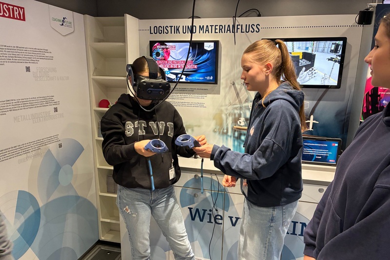 Bild 2: Schülerin testet eine VR-Brille, eine Mitschülerin unterstützt sie